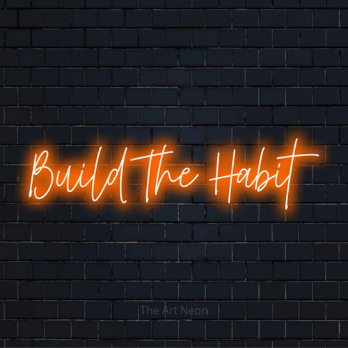 "Build The Habit" LED neon sign on a black brick wall