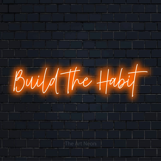 "Build The Habit" LED neon sign on a black brick wall