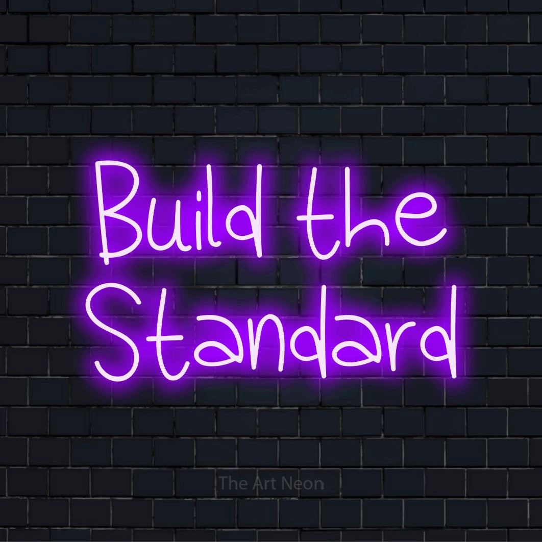 "Build The Standard" script-style LED neon sign on a black brick wall
