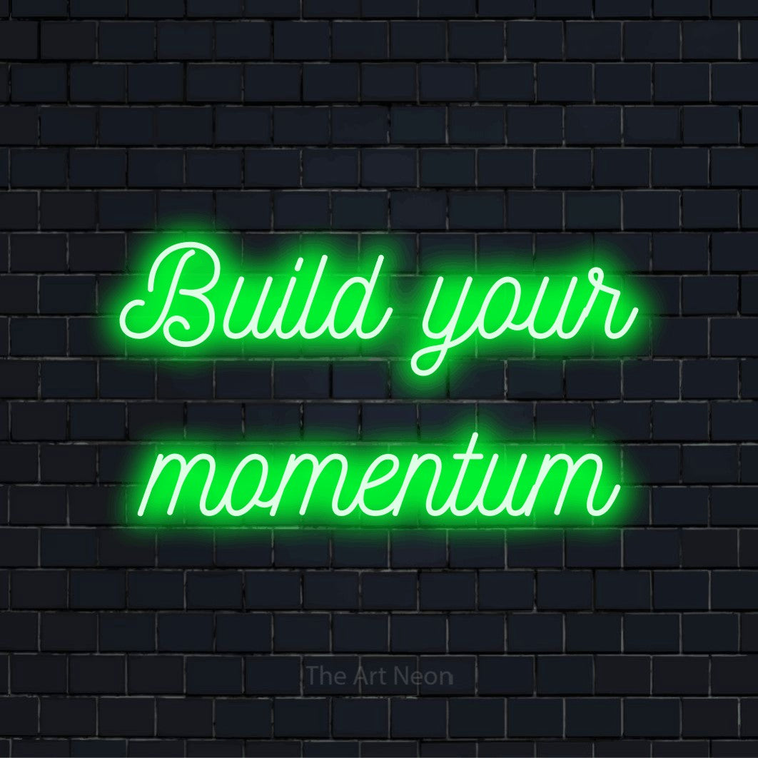"Build Your Momentum" script-style LED neon sign on a black brick wall