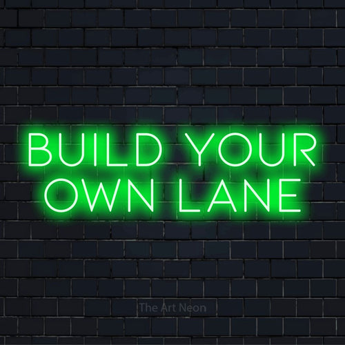 "Build Your Own Lane" LED neon sign on a black brick wall