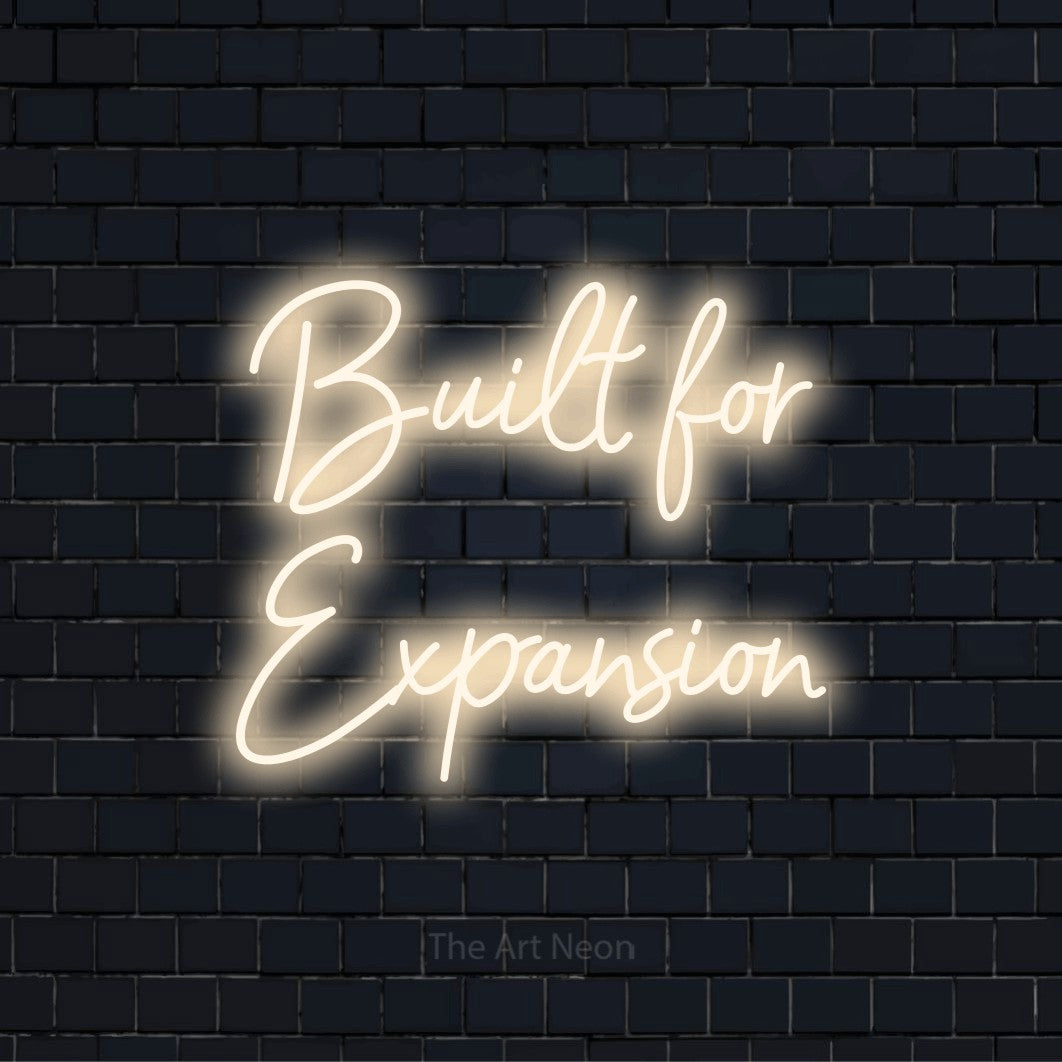 "Built For Expansion" glowing LED neon sign on a black brick wall