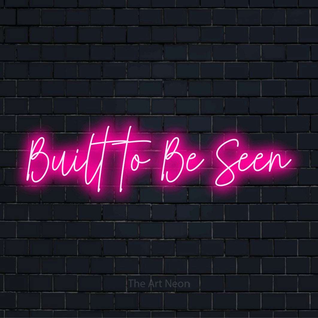 "Built To Be Seen" text design with neon effect on a black brick wall