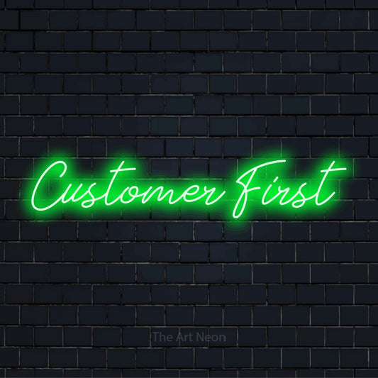 "Customer First" script-style LED neon sign on a black brick wall