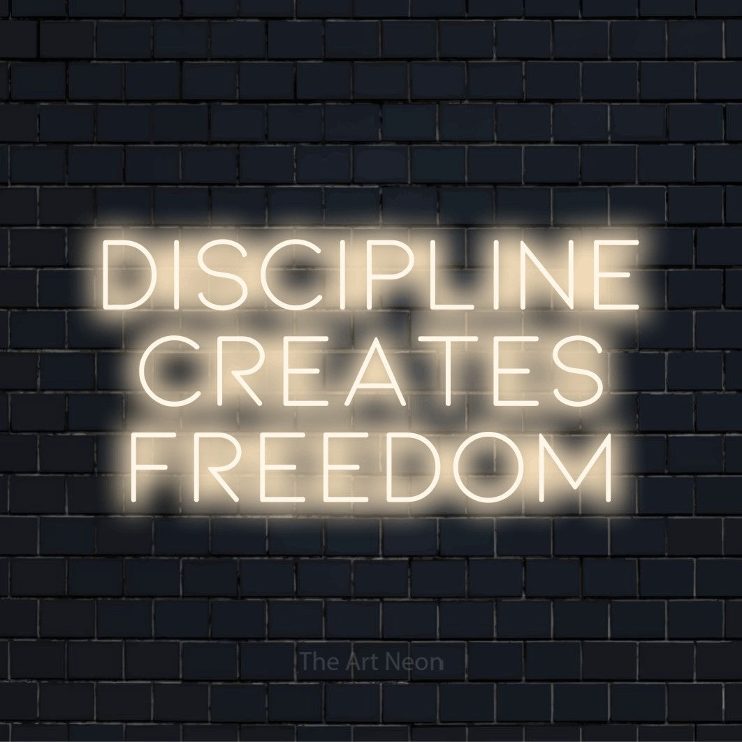 "Discipline Creates Freedom" glowing LED neon sign on a black brick wall