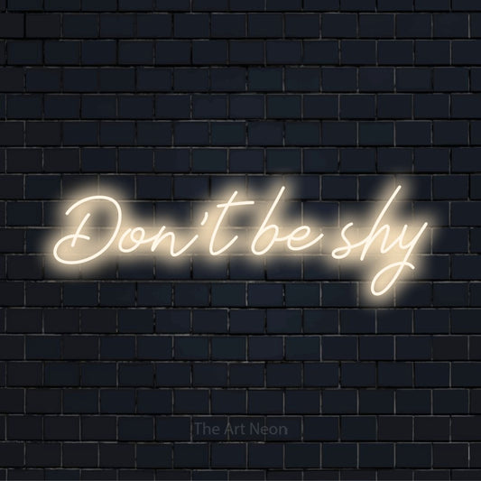 "Don’t Be Shy" LED neon sign on a black brick wall