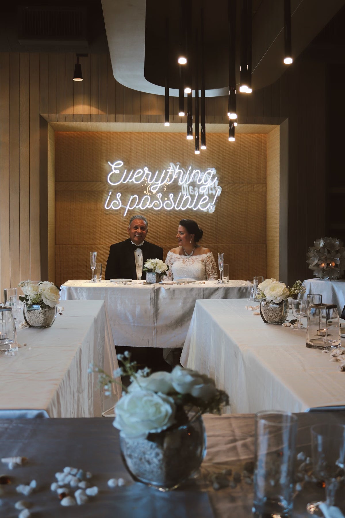 Script LED neon phrase glowing above a wedding reception table