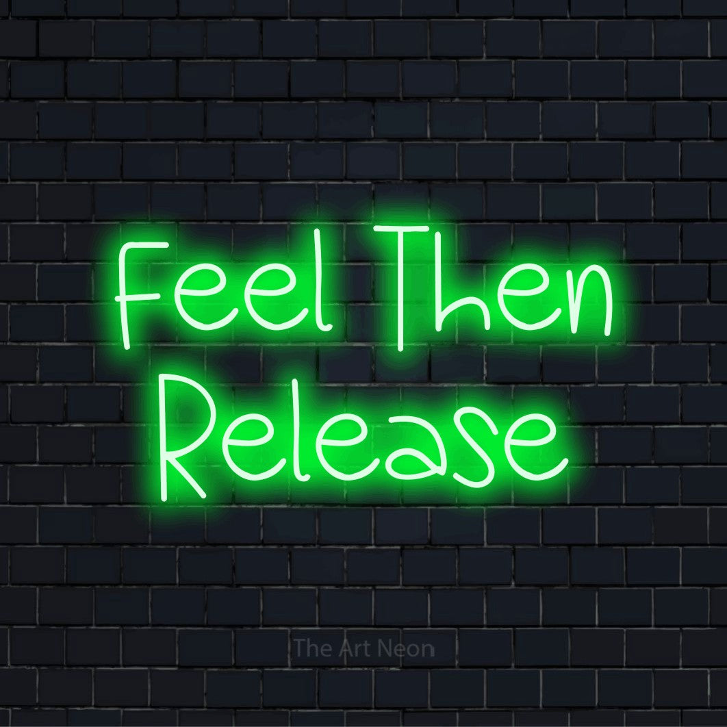 "Feel Then Release" script-style LED neon sign on a black brick wall