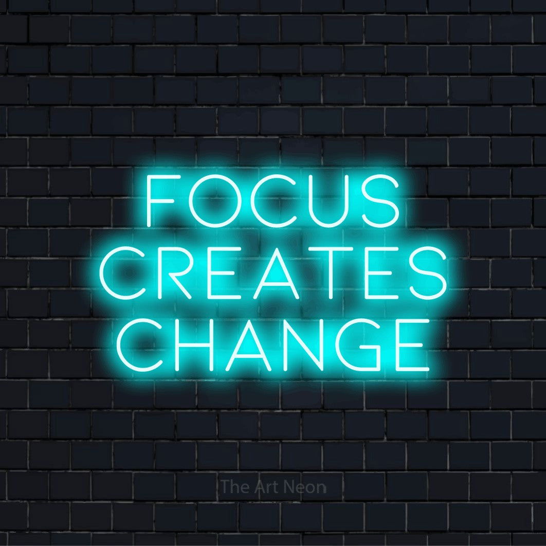 "Focus Creates Change" glowing LED neon sign on a black brick wall