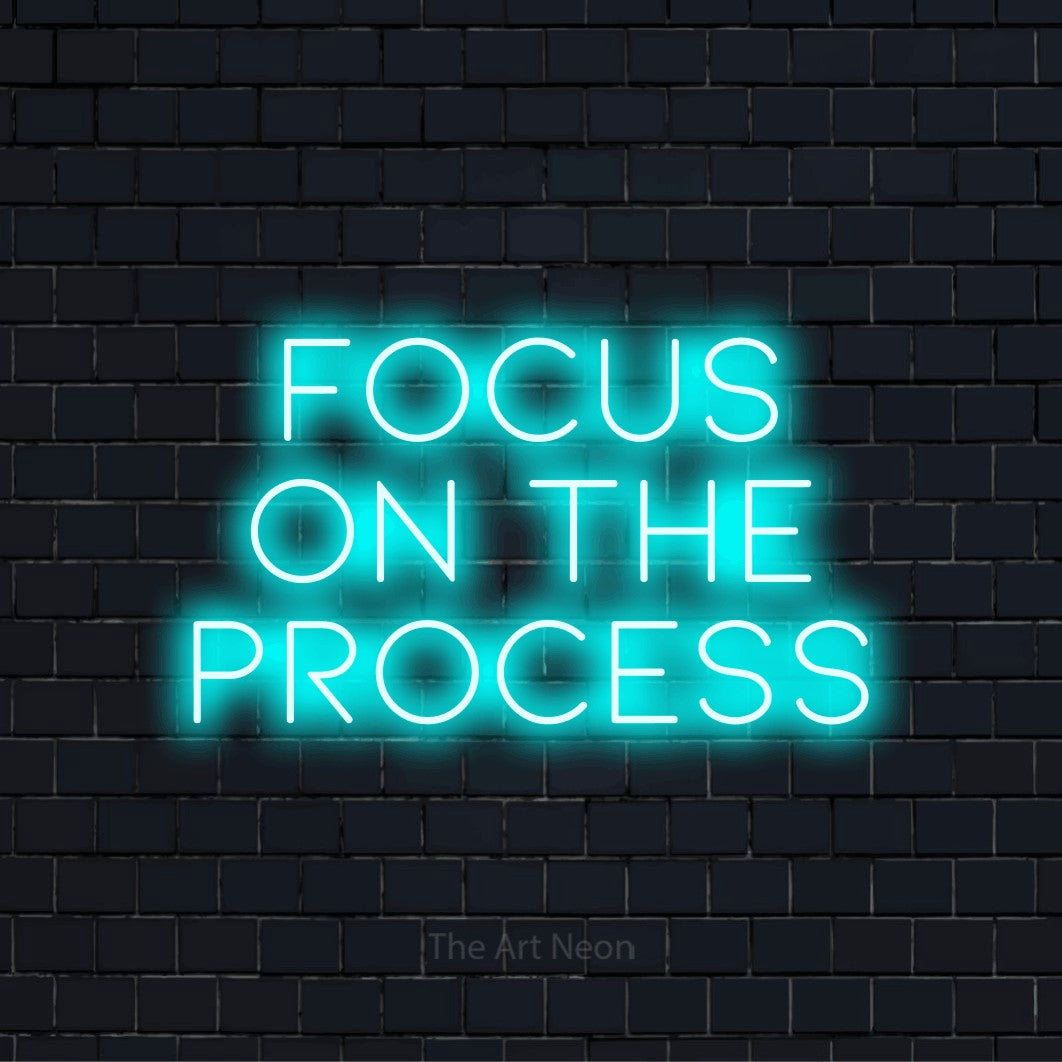 "Focus On The Process" script-style LED neon sign on a black brick wall