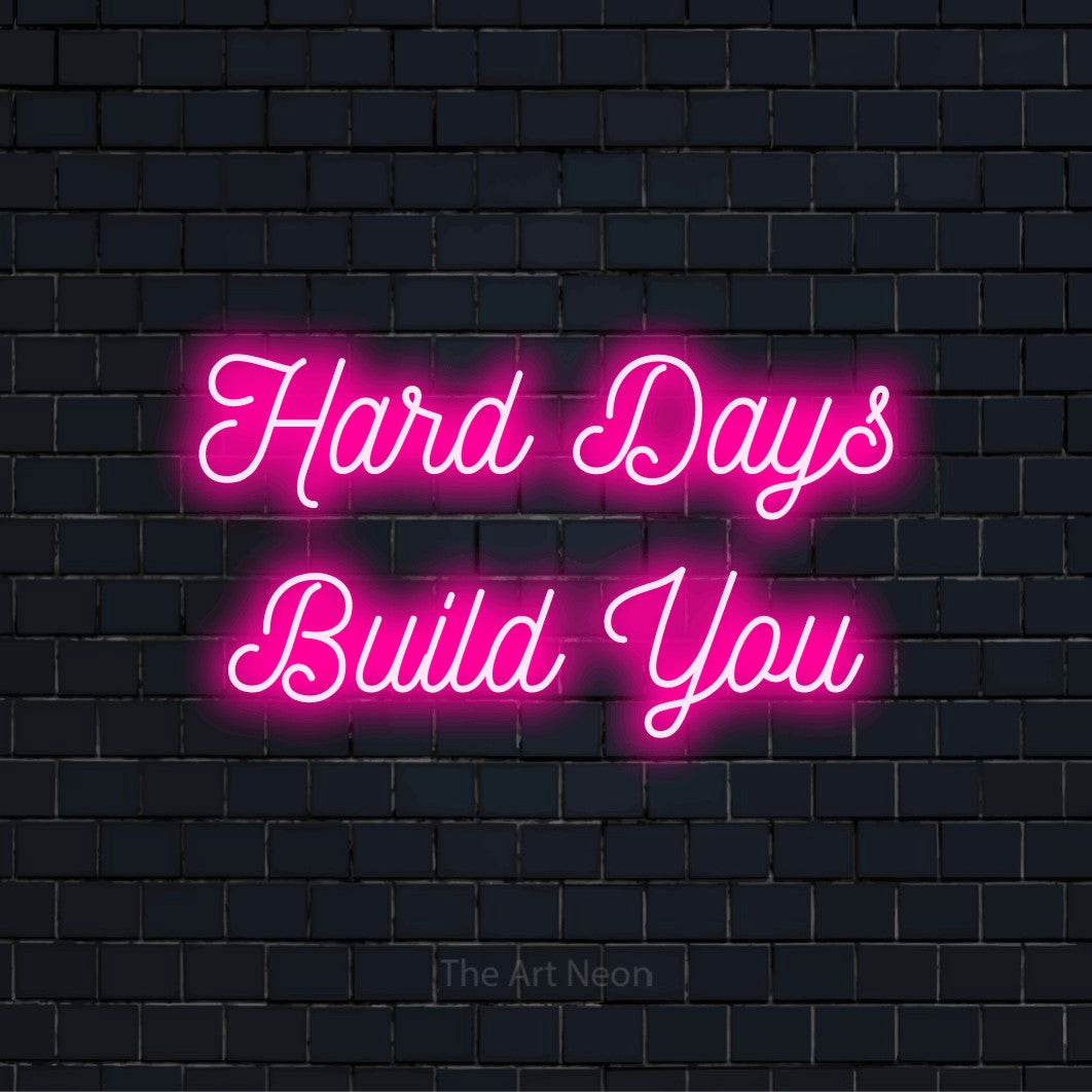 "Hard Days Build You" text design with neon effect on a black brick wall