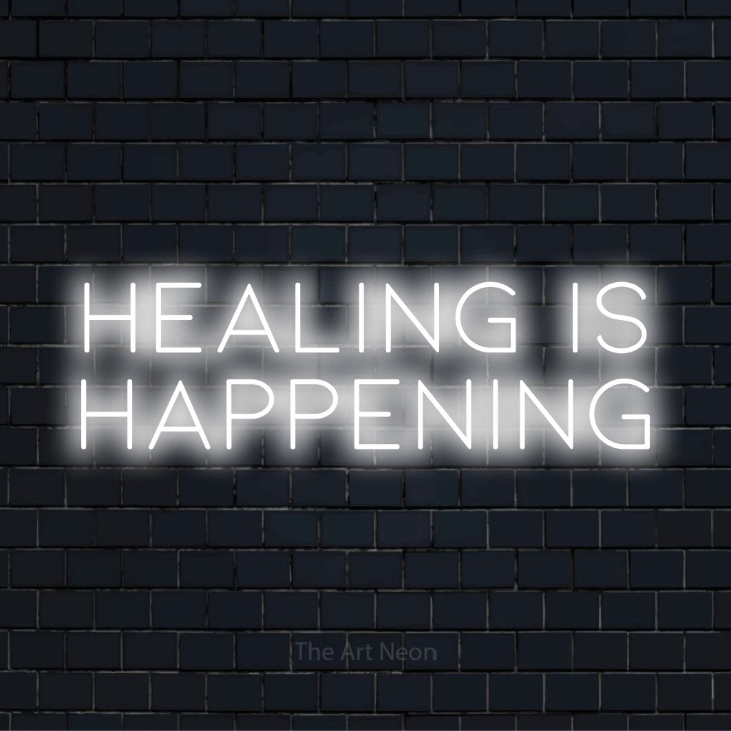 "Healing Is Happening" neon text design on a black brick wall