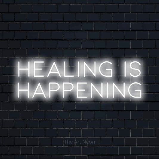 "Healing Is Happening" neon text design on a black brick wall