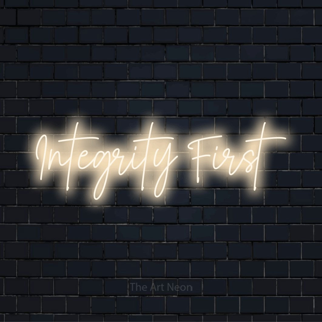 "Integrity First" script-style LED neon sign on a black brick wall