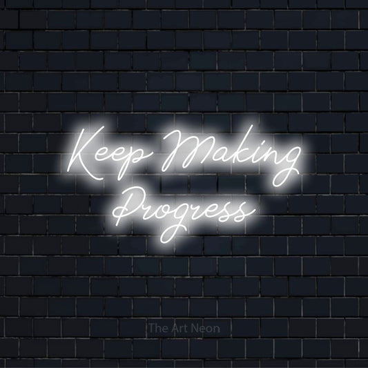 "Keep Making Progress" script-style LED neon sign on a black brick wall