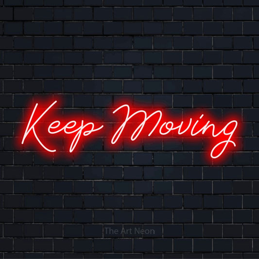 "Keep Moving" script-style LED neon sign on a black brick wall
