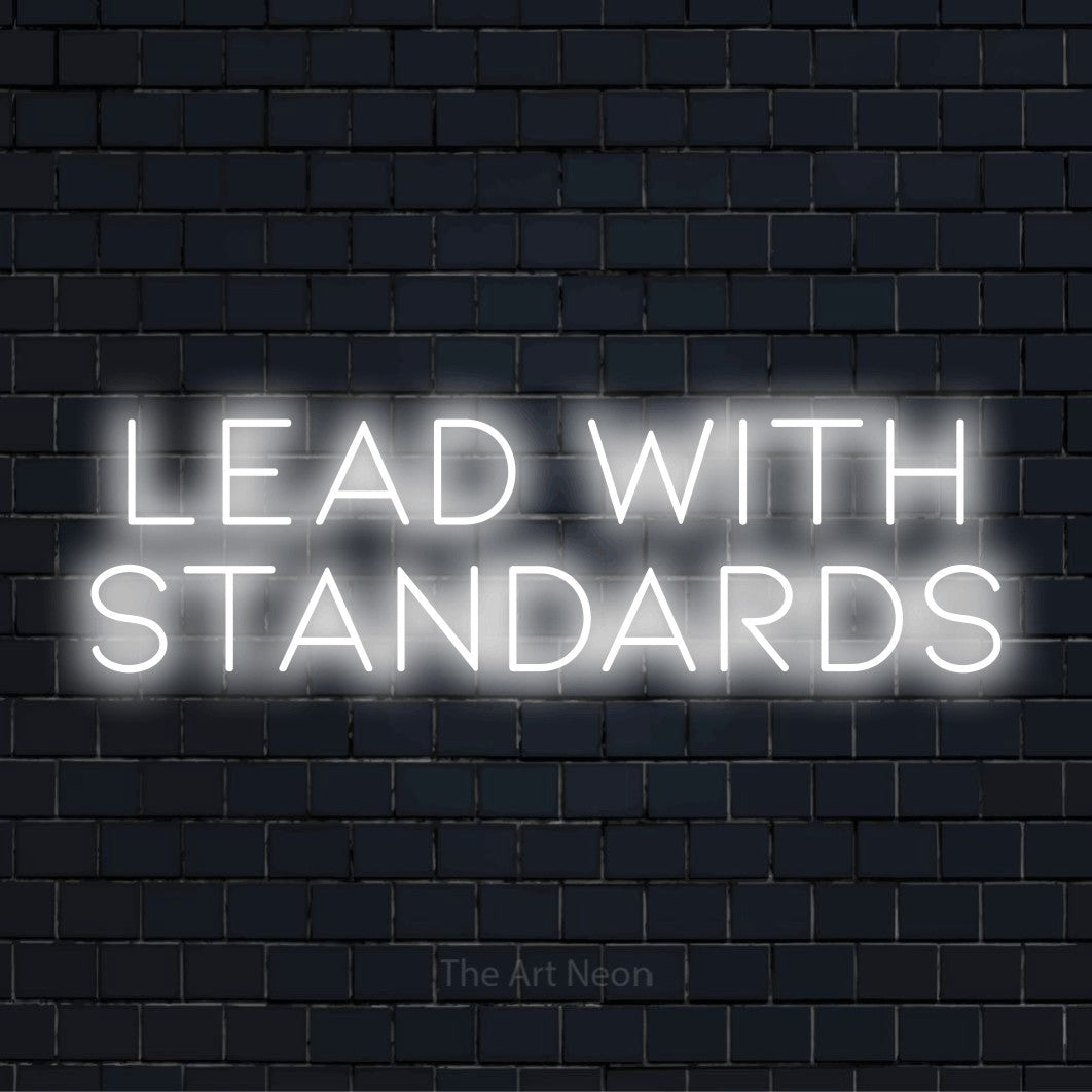 "Lead With Standards" glowing LED neon sign on a black brick wall