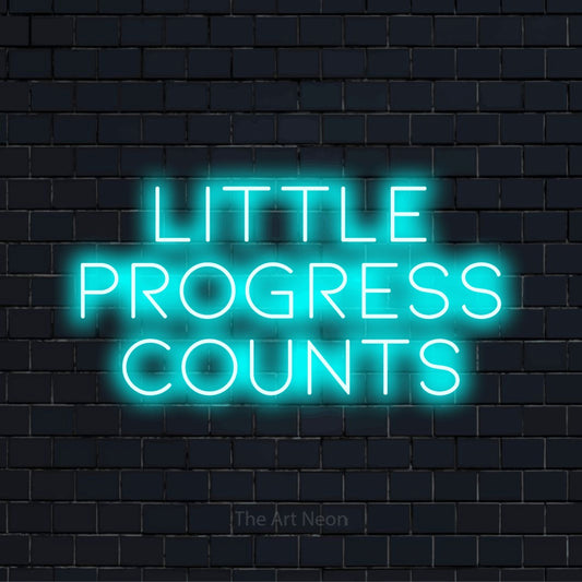 "Little Progress Counts" glowing LED neon sign on a black brick wall