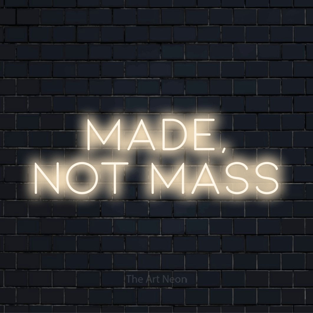 "Made, Not Mass" text design with neon effect on a black brick wall