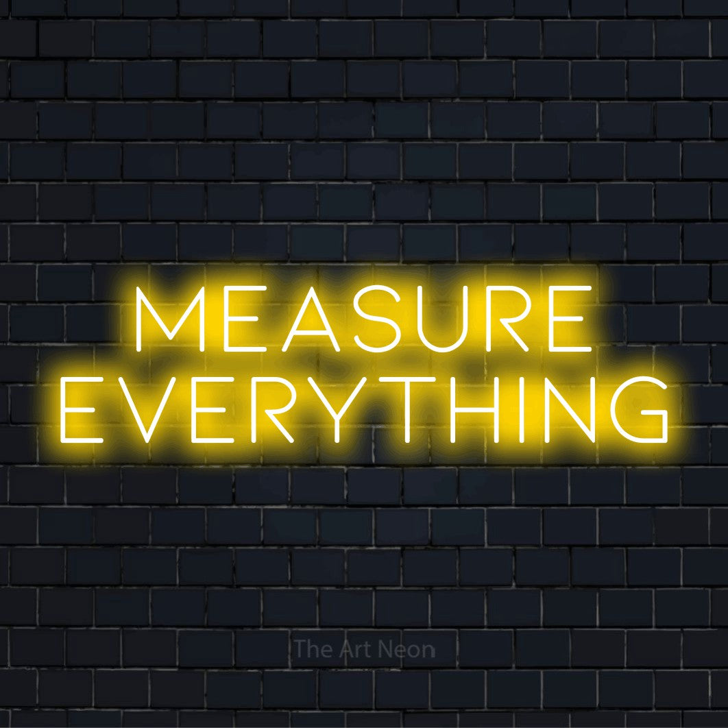 "Measure Everything" LED neon sign on a black brick wall