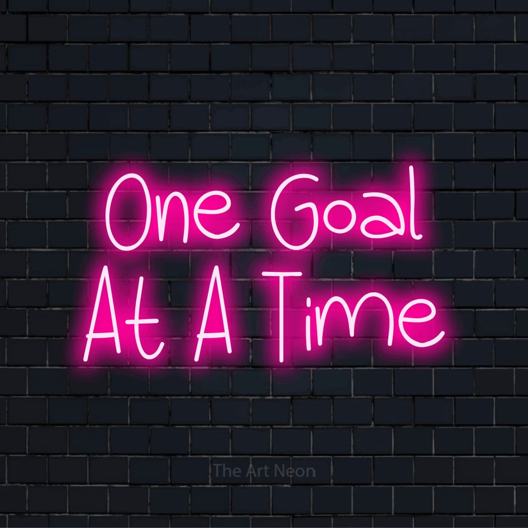 "One Goal At A Time" text design with neon effect on a black brick wall
