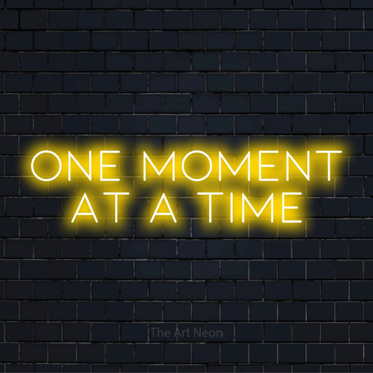 "One Moment At A Time" LED neon sign on a black brick wall