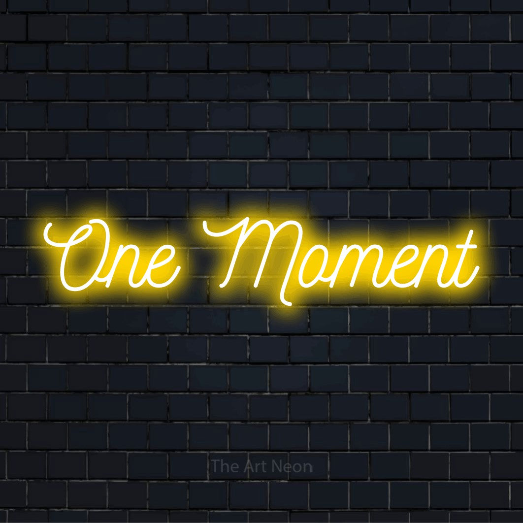 "One Moment" script-style LED neon sign on a black brick wall