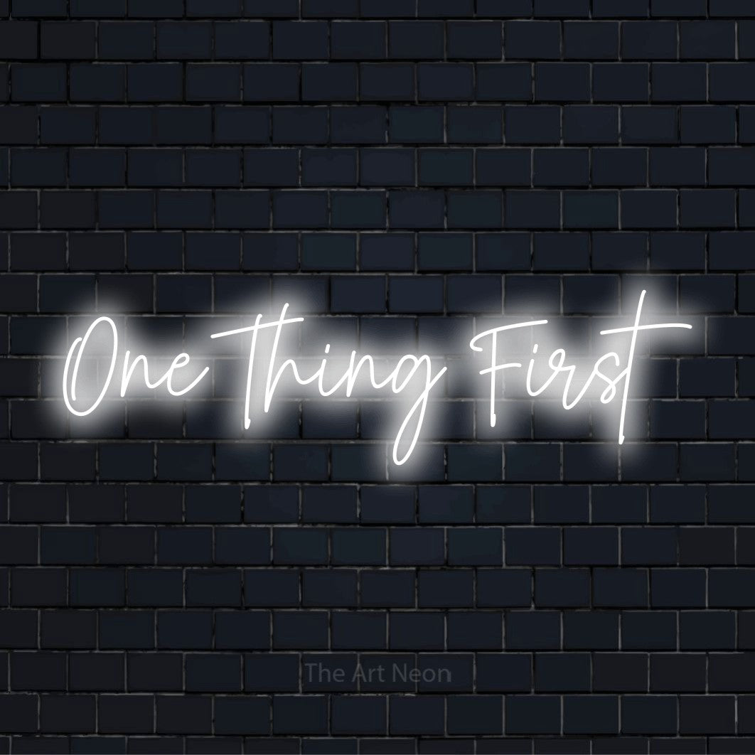 "One Thing First" glowing LED neon sign on a black brick wall