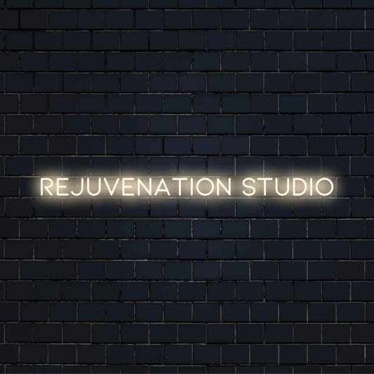 Rejuvenation Studio Neon Sign, glowing lettering on dark brick wall