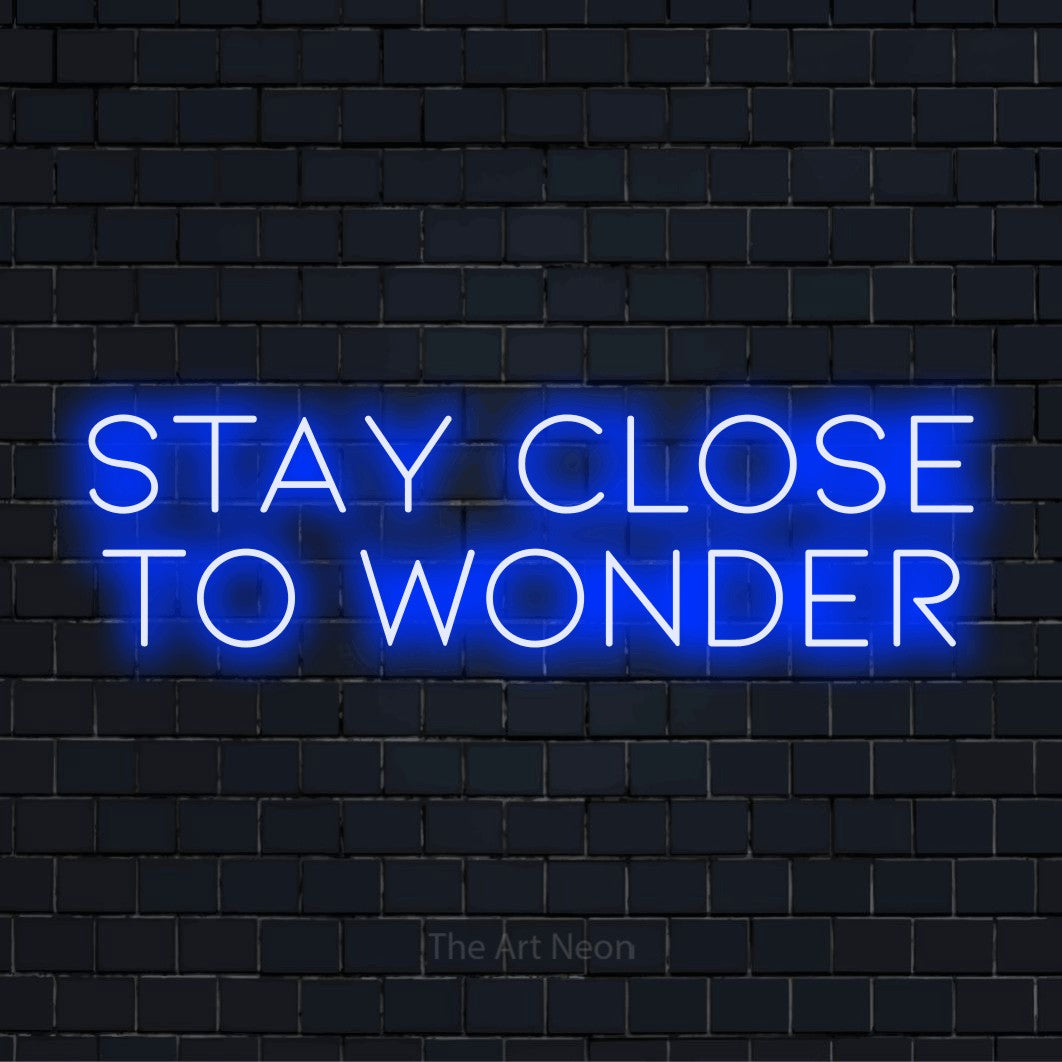 "Stay Close To Wonder" neon text design on a black brick wall