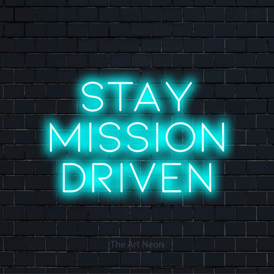 "Stay Mission Driven" script-style LED neon sign on a black brick wall