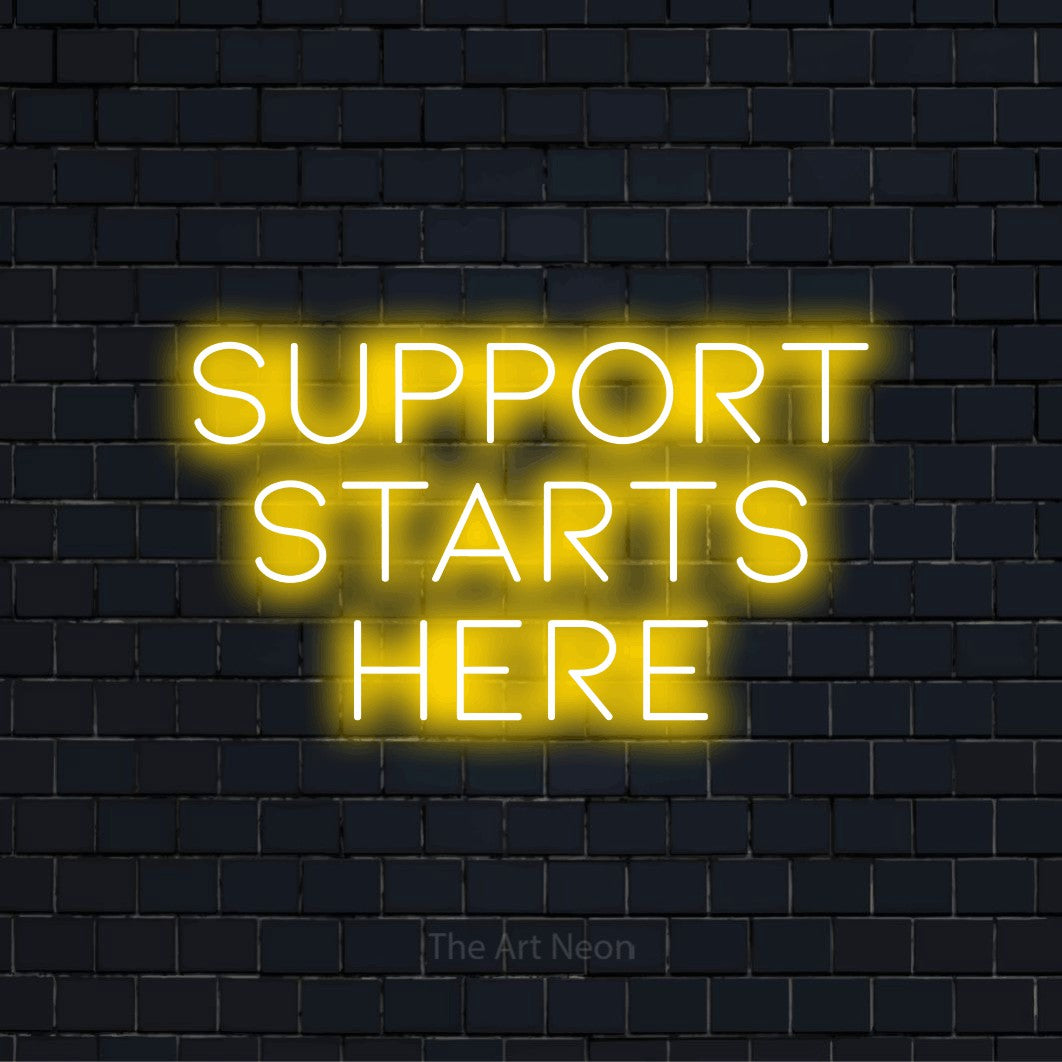 "Support Starts Here" script-style LED neon sign on a black brick wall