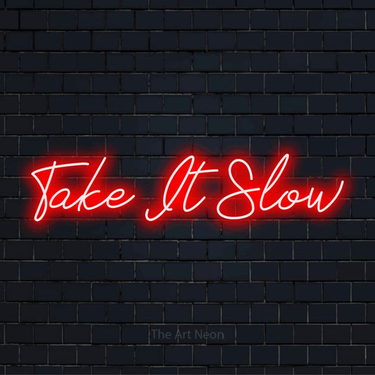 "Take It Slow" text design with neon effect on a black brick wall