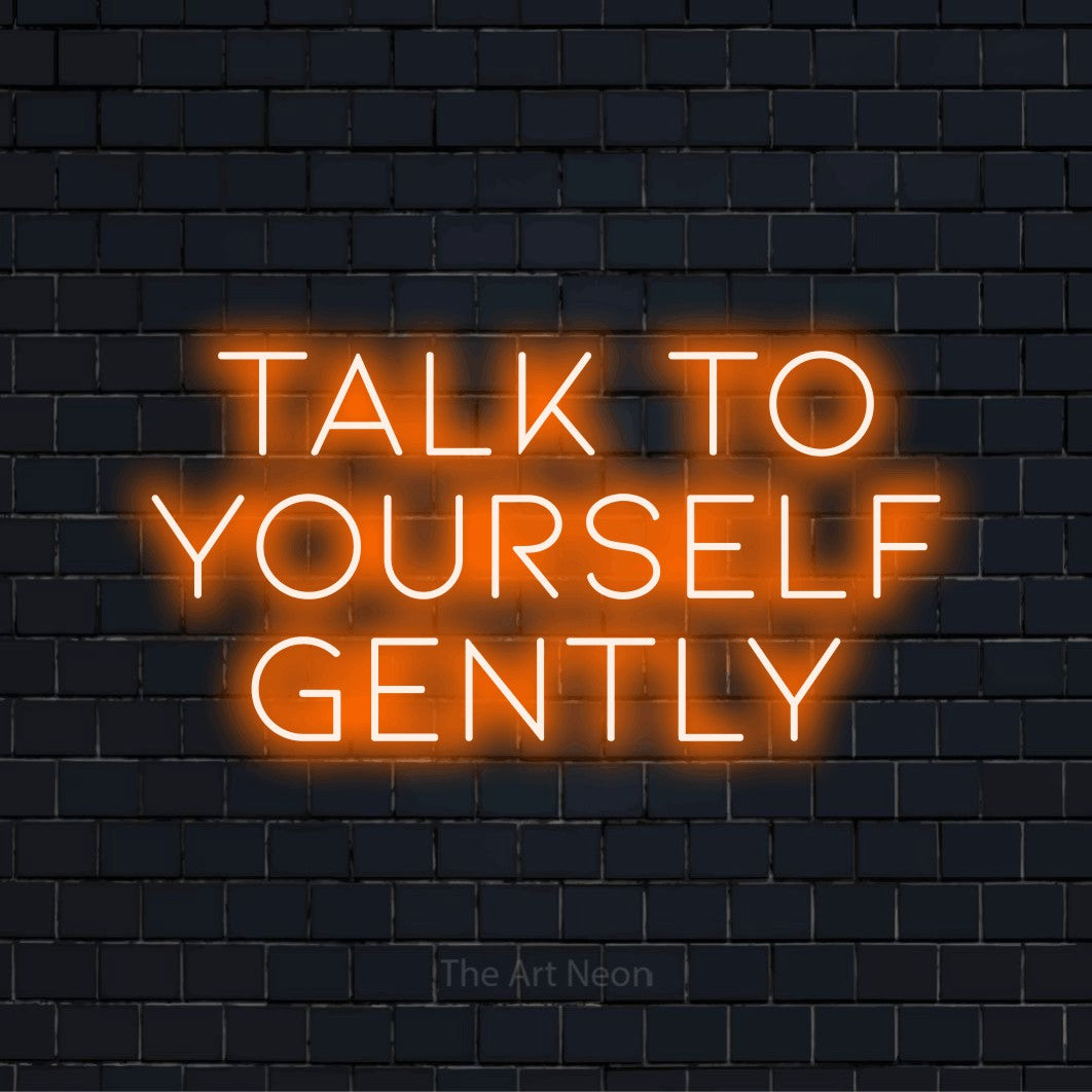 "Talk To Yourself Gently" neon text design on a black brick wall