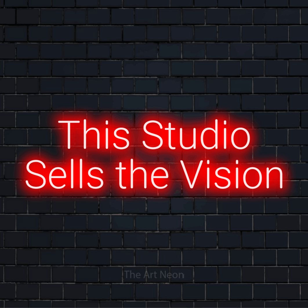 "This Studio Sells The Vision" glowing LED neon sign on a black brick wall