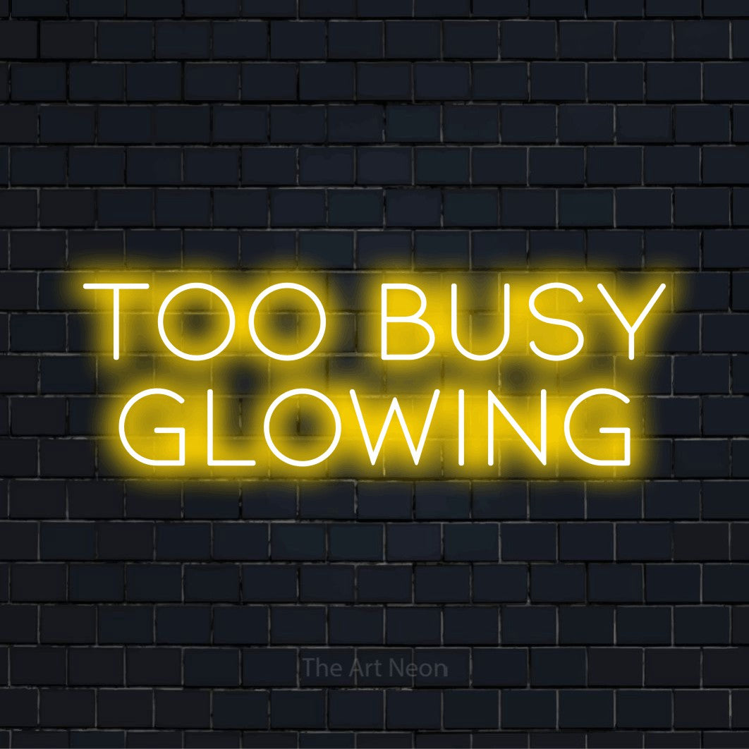 "Too Busy Glowing" neon text design on a black brick wall