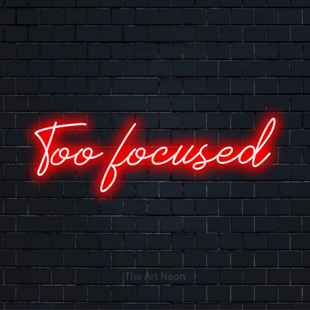 "Too Focused" glowing LED neon sign on a black brick wall