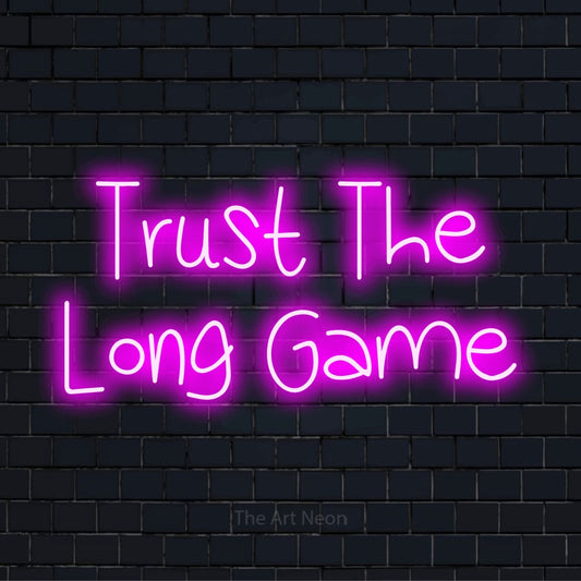 "Trust The Long Game" text design with neon effect on a black brick wall