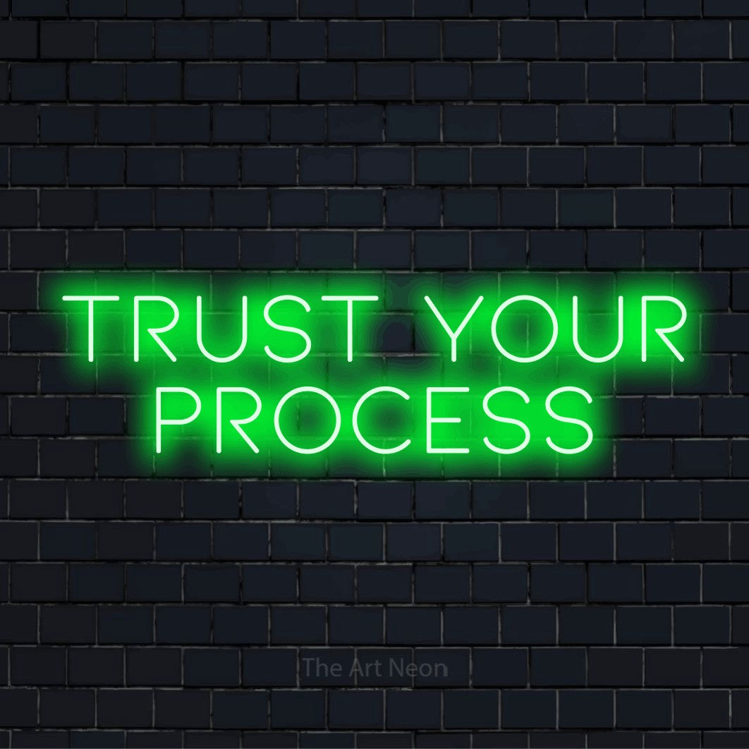 "Trust Your Process" glowing LED neon sign on a black brick wall