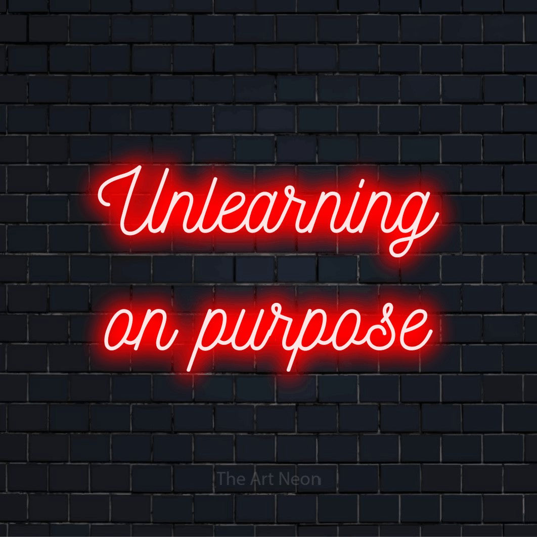 "Unlearning On Purpose" neon text design on a black brick wall
