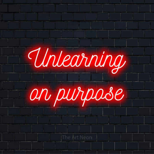 "Unlearning On Purpose" neon text design on a black brick wall