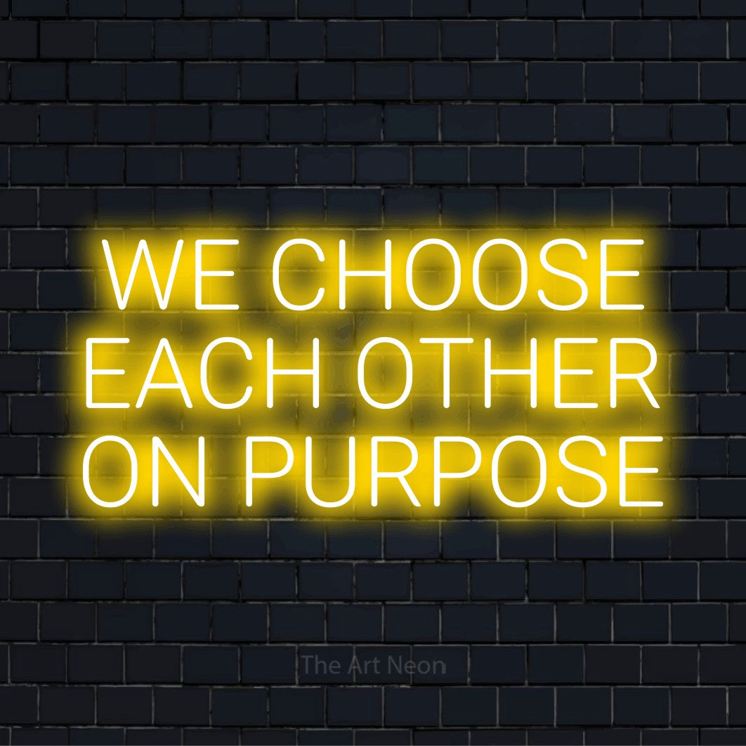 "We Choose Each Other On Purpose" script-style LED neon sign on a black brick wall