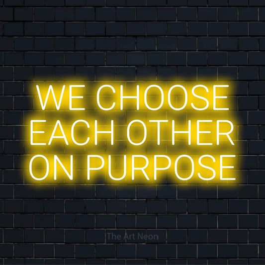 "We Choose Each Other On Purpose" script-style LED neon sign on a black brick wall