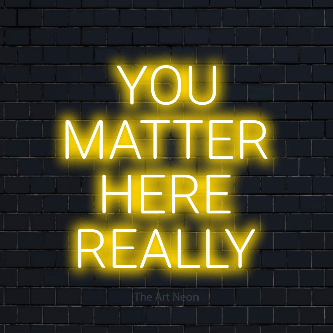 "You Matter Here Really" script-style LED neon sign on a black brick wall