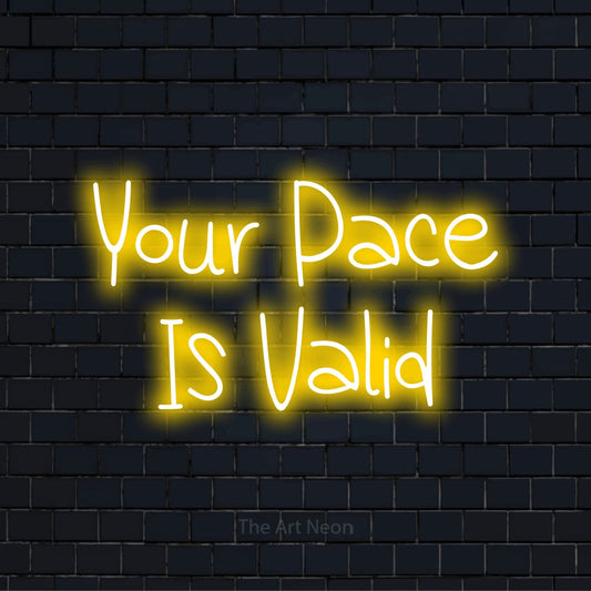 "Your Pace Is Valid" neon text design on a black brick wall