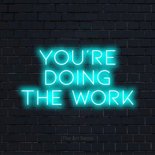 "You’re Doing The Work" text design with neon effect on a black brick wall