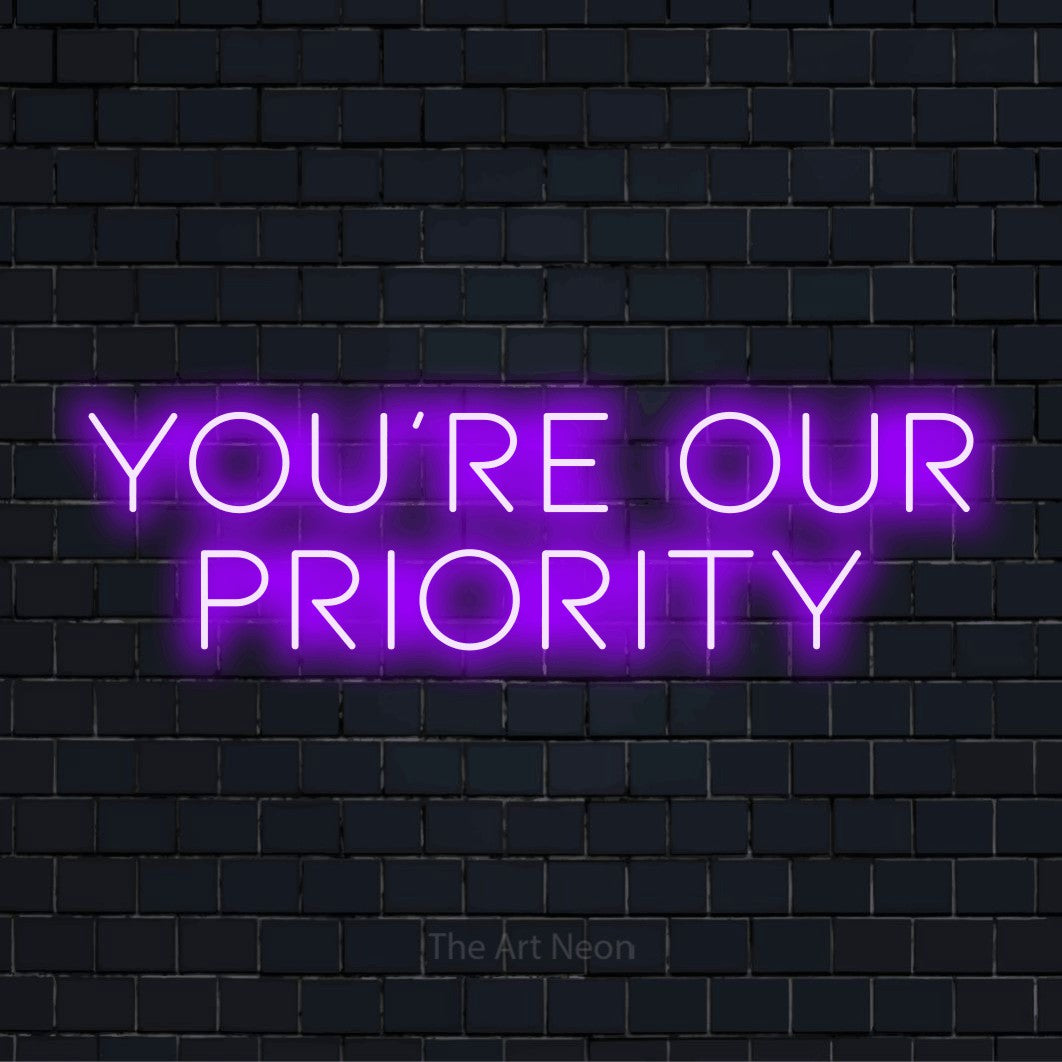 "You’re Our Priority" script-style LED neon sign on a black brick wall